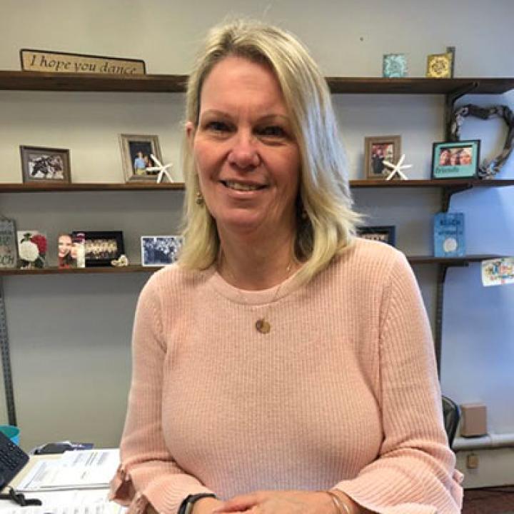 Maureen Colgan wearing a pink sweater with an office behind her