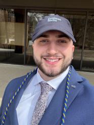 Evan Glusic wearing a suit and a Goldman Sachs baseball cap.